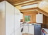 Küche in einem Holzhaus mit weißen Schränken, Waschmaschine, Spüle am Fenster und sichtbaren Holzbalken an der Decke.