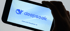 Das Bild zeigt eine Hand, die ein Smartphone hält. Auf dem Bildschirm ist das DeepSeek-Logo zu sehen: ein stilisierter, blauer Wal gefolgt vom Schriftzug "deepseek". Unter dem Logo steht der Text "Chat with DeepSeek AI". Der Hintergrund des Bildschirms ist ein helles Blau mit sanften Wellenlinien.