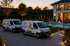 Zwei weiße Transporter mit Firmenlogo "Starke" stehen vor einem modernen Haus mit beleuchtetem Pool bei Dämmerung.