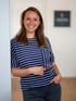 Junge Frau mit braunen Haaren, gestreiftem Oberteil und Jeans, die lächelt und eine Brille hält.