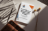 Ein weißes E-Book mit dem Titel "7 Schritte zum strategischen Werbemittel-Einkauf" liegt auf einem Tisch neben einem Notizbuch und Stift.
