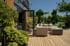 Moderne Holzterrasse mit beigem Ecksofa, Couchtisch und Blick auf einen Garten mit Bonsai-Bäumen und Formgehölzen.
