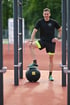 Mann in Sportkleidung steht mit einem Fuß auf einem schwarzen Medizinball mit gelbem TRX-Logo.