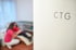 Tür mit Aufschrift "CTG", unscharfer Hintergrund mit Hebamme und schwangerer Frau auf einer Liege.