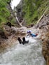 Person in Neoprenanzug rutscht im Wildwasser durch eine felsige Schlucht.