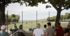 Zuschauer beobachten ein Fußballspiel auf einem grünen Feld unter Bäumen.