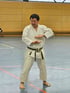Keigo Shimizu Sensei in weißem Karate-Gi und schwarzem Gürtel steht barfuß in einer Turnhalle und hält seine Hände vor sich.