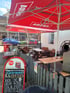 Biergarten mit roten Astra-Sonnenschirmen und einem Schild "Getränke & Speisen".
