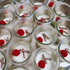 Viele kleine Gläschen mit weißer Creme, Himbeeren und Schokoröllchen.