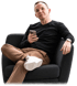 Ein Mann mit Smartphone sitzt in einem dunklen Sessel vor schwarzem Hintergrund und trägt einen schwarzen Pullover.