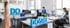 Mitarbeiter arbeiten an Schreibtischen in einem hellen Büro mit blauen 3D-Buchstaben der Aufschrift DOGREL.