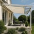 Moderne Terrassenüberdachung mit weißem Gestell, beigem Stoffdach und Glassegmenten über einem Gartentisch.