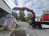 Ein roter Fassi-Ladekran auf einem LKW hebt eine mit weißer Folie verpackte Maschine vor einem Gebäude an.