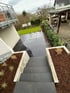 Moderne Außentreppe aus dunklen Steinplatten führt hinunter zu einer passenden Terrasse mit angrenzender Rasenfläche.