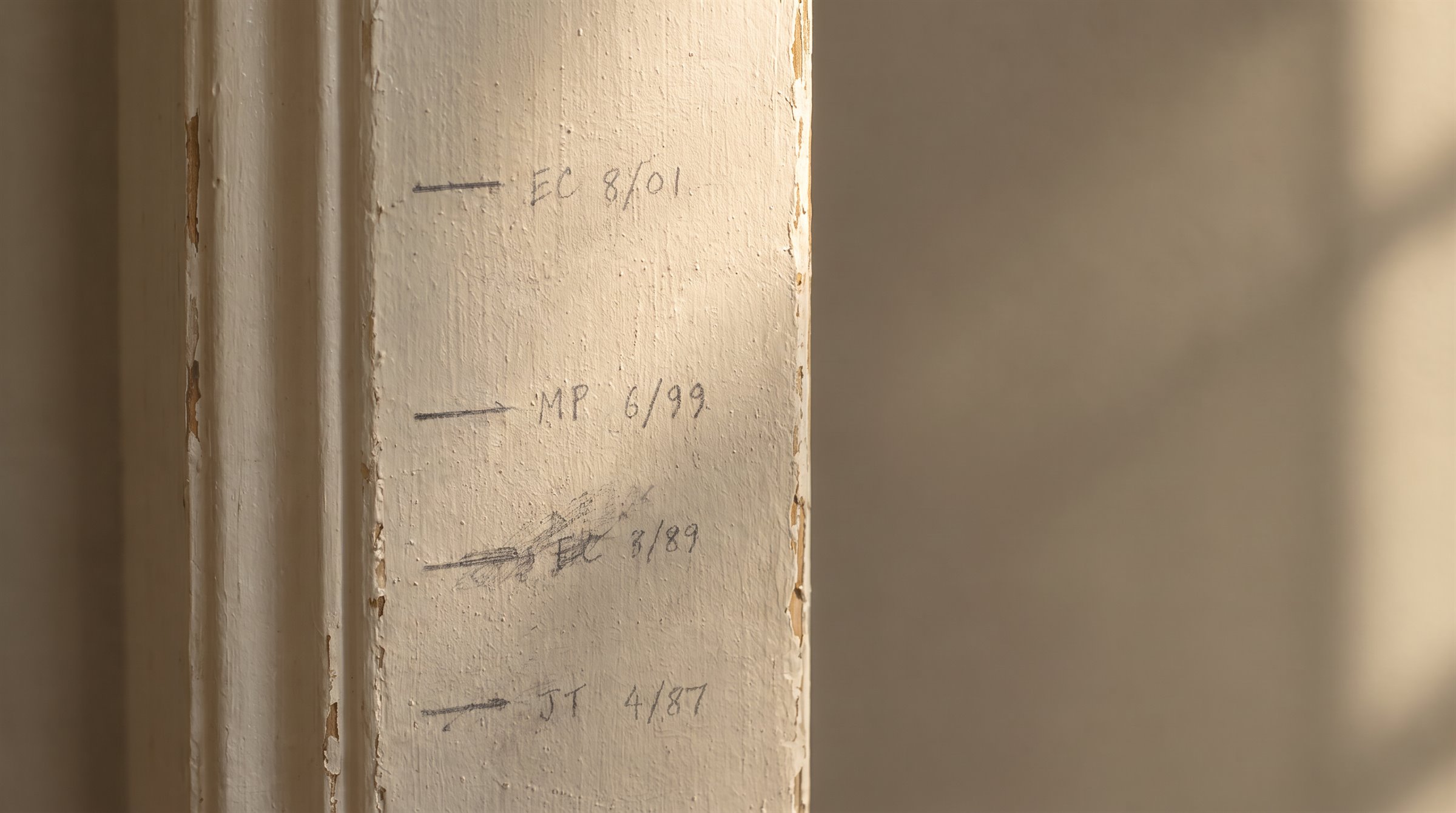 Pencil height marks on a painted doorframe, each with initials and a date.