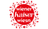 Logo der Wiener Kaiser Wiesn mit weißem Text auf rotem Kreis, umrahmt von einem roten Blumenkranz auf schwarzem Grund.