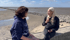 Zwei Frauen sitzen auf einer Steinmauer im Wattenmeer und unterhalten sich bei sonnigem Wetter.