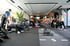 Mehrere Personen trainieren in einem modernen Fitnessstudio, mit Hantelbänken, Gewichten, einem Boxsack und Trainingsgeräten.