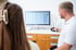 Ein Mann zeigt einer Patientin eine medizinische Analyse mit menschlichen Körpersilhouetten auf einem Computerbildschirm.