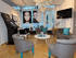 Moderner Beauty-Salon mit grauen Sesseln, weißem Couchtisch, Schminkstation und Porträtfotos an den Fenstern.