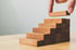 Hand platziert Holzklotz auf einer Treppe aus Holzklötzen, die nach oben führt.