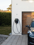 Schwarze Wallbox mit grünem Licht an weißer Hauswand, lädt ein dunkles Elektroauto.