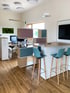 Modernes Büro mit Holzboden, buntem Raumteiler-Regal, Stehtisch mit blauen Barhockern und Monitor an der Wand.