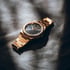 Goldene Armbanduhr mit dunklem Zifferblatt auf grauem Stoff, mit Schattenwurf.