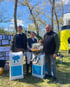 Drei Erwachsene und ein Kind stehen neben zwei Bluefrog-Säcken und halten ein Geschenkpaket in einem Park.