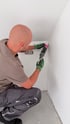 Handwerker trägt mit einer Kartuschenpresse weißes Silikon oder Acryl in die Wandecke eines Raumes auf.