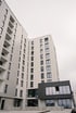 Modern white apartment buildings with dark windows and a gray ground-floor facade under a cloudy sky.