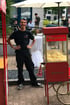 Ein lächelnder junger Mann steht neben einem roten Popcorn-Wagen mit dem Schriftzug "Popcorn".