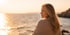 Blonde Frau blickt bei Sonnenuntergang auf das Meer hinaus.