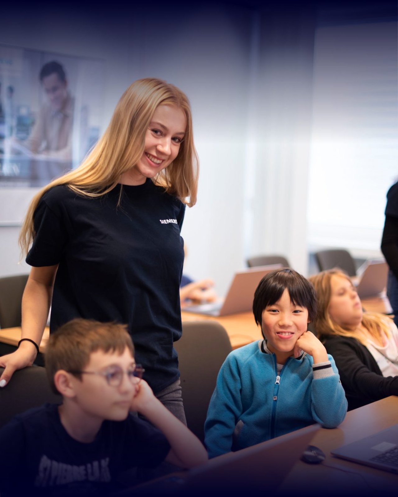 Kinder lernen in einem Code Camp gemeinsam am Laptop programmieren, begleitet von einer Trainerin