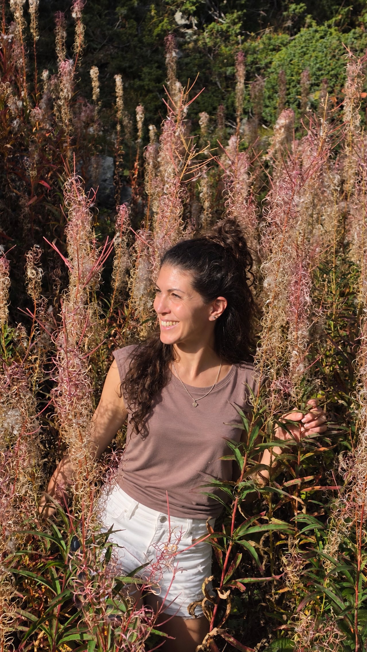 Seraina Grob lachend inmitten von hohen, verblühten Weidenröschen in der Sonne