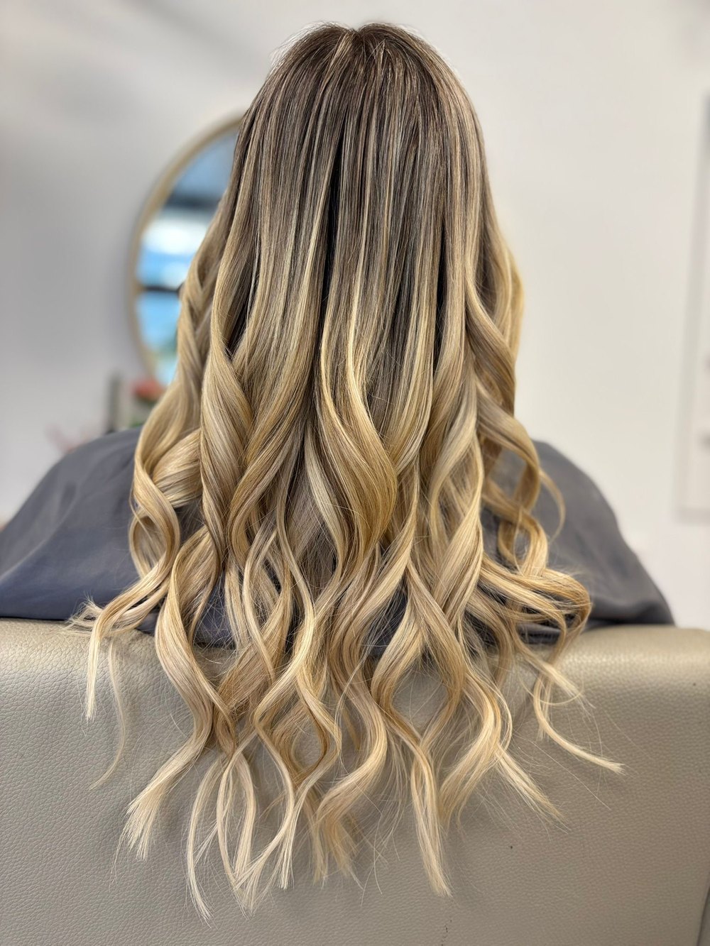 Schulterlanges blondes Haar mit dunklem Ansatz, nachher lange gewellte Balayage