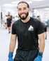 Arham - Boxtrainer BACKYARD Wien - Trainer lächelt in die Kamera während im Hintergrund das Gruppenboxtraining stattfindet
