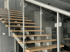 Eine moderne Holztreppe mit Glasgeländer und silbernen Metallpfosten.