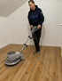 Mann poliert einen Holzboden mit einer großen, grauen Poliermaschine.