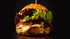 Großer Gourmet-Burger mit Salat, Tomate, Soße, Käse und Rindfleisch auf einem Holzbrett.