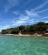 Türkisfarbenes Wasser neben einer felsigen Küste mit grünen Büschen unter blauem Himmel mit weißen Wolken in Drage Kroatien.
