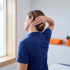 Woman in a blue polo shirt performs a neck stretch by tilting her head and placing her hand on her neck.