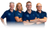 Vier lächelnde Personen in dunkelblauen Poloshirts mit einem Logo stehen mit verschr änkten Armen.