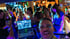 DJ in einer Bar mit Laptop und DJ-Software vor einer tanzenden Menge bei blauem und grünem Licht.