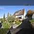 Weißes Einfamilienhaus mit braunem Ziegeldach, Vorgarten und Auffahrt unter blauem Himmel.