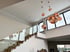 Helle moderne Treppe mit Glasgeländer und hängenden orangefarbenen Deckenlampen in einem großen Raum mit Fenstern.