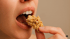 Nahaufnahme einer Person, die sich ein knuspriges Müsli-Cluster in den Mund schiebt.