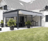Eine moderne graue Pergola mit ausziehbarer Markise über einer Terrasse mit Möbeln und Pflanzen.