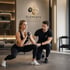 Frau macht Ausfallschritte mit Kettlebell, Personal Trainer korrigiert Haltung. Logo "ELEMENTS" im Hintergrund.