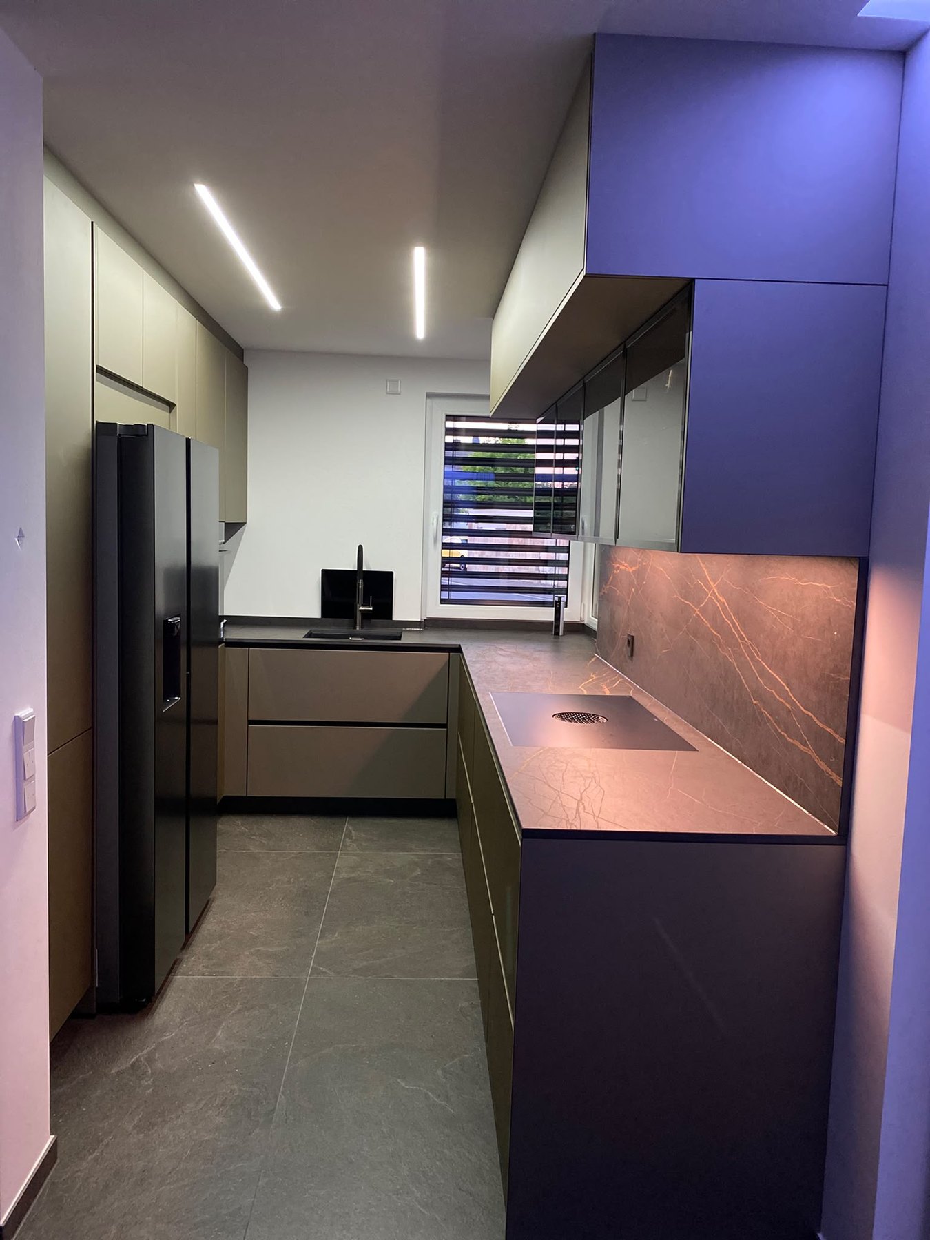 Blick in die olivgrüne Küche mit Side-by-Side-Kühlschrank und durchgehender Arbeitsfläche